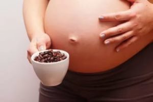беременная женщина держит чашку кофе